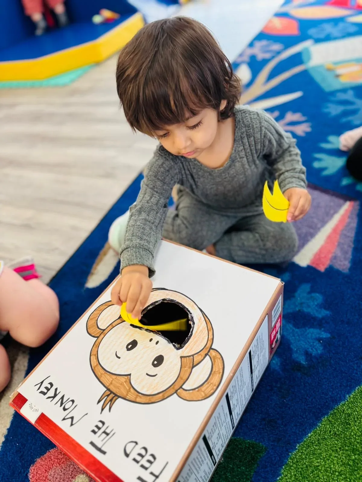A toddler posting paper bananas into a homemade Feed the Monkey counting game