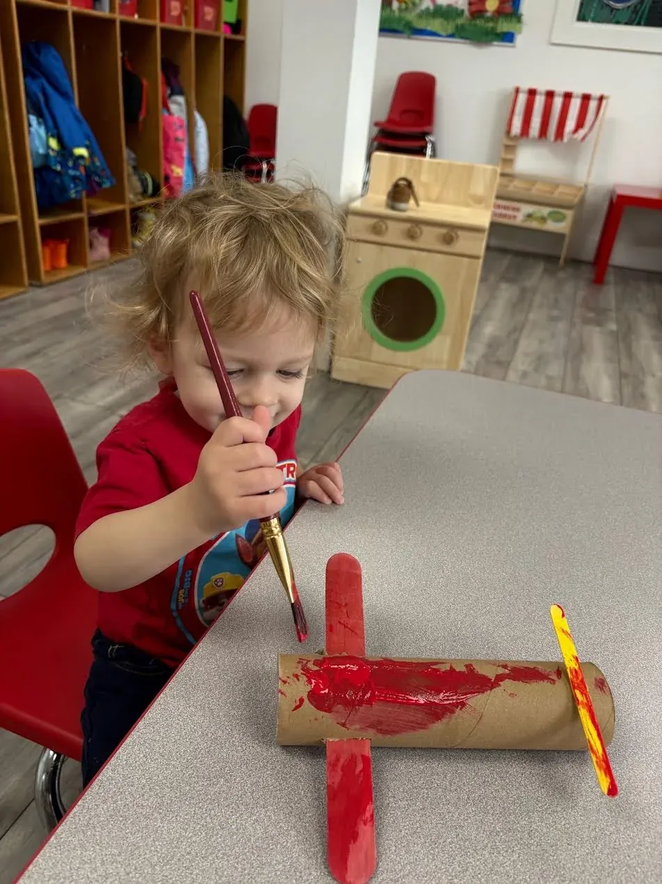 A child painting a handmade cardboard-tube airplane craft red