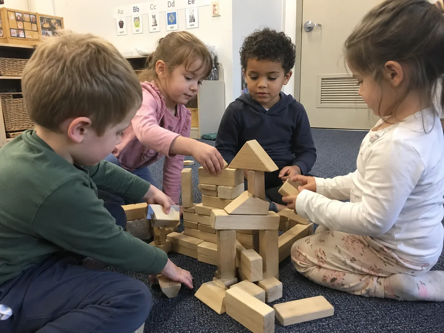 Four children building a tall tower together with wooden blocks