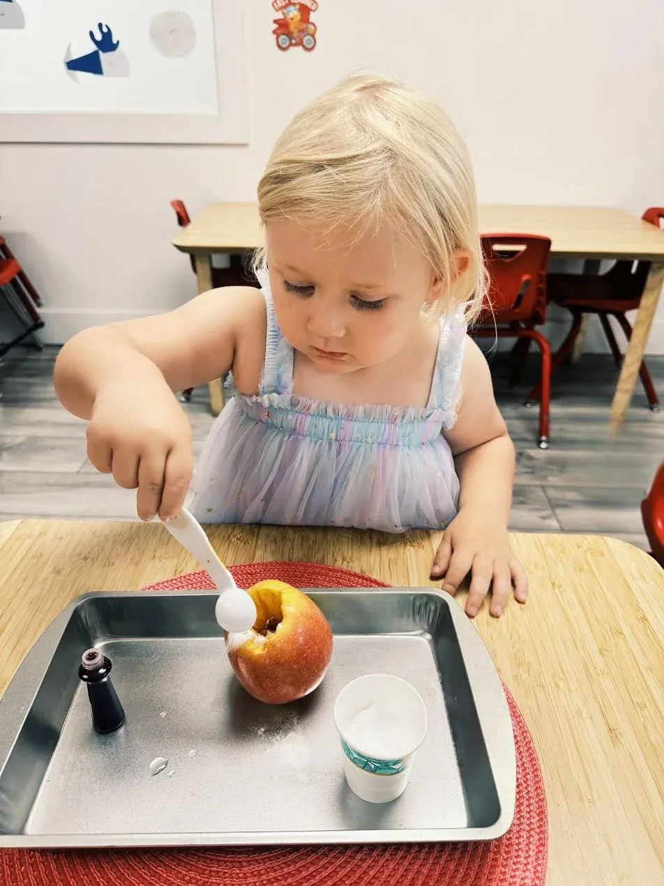 A child carefully spooning baking soda into an apple during a science experiment