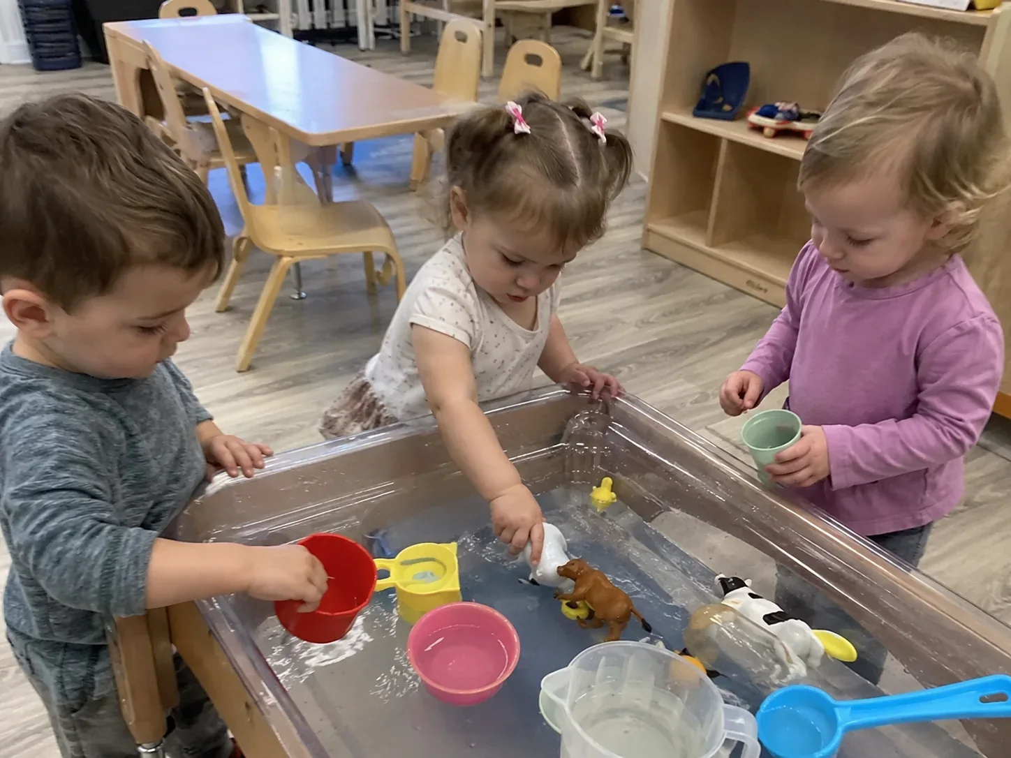 Three toddlers exploring animals and cups together at a water sensory table